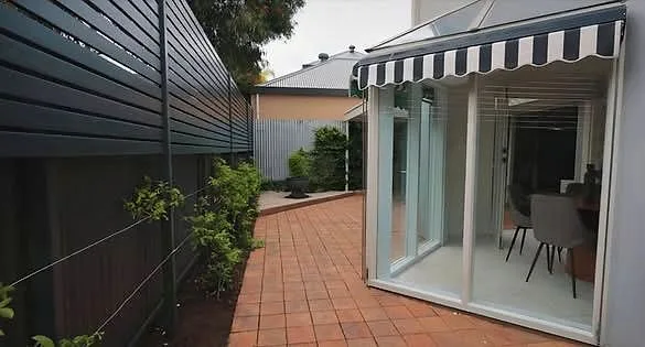 Dark slat fence and gate running alongside a brick paved path